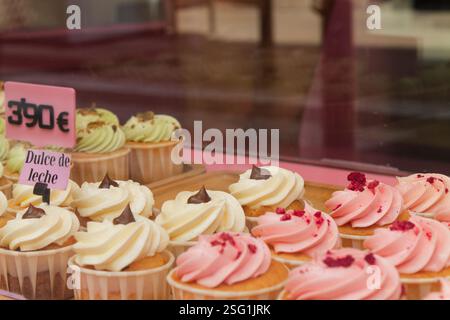 Un'esposizione di cupcake colorati in una finestra di panetteria, con vortici di glassa in bianco, rosa e verde. Alcuni cupcake sono ricoperti di cioccolato chi Foto Stock