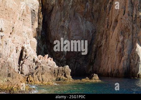 Una scogliera costiera rocciosa con pareti ripide e acqua cristallina alla base. La consistenza delle rocce è aspra e presenta formazioni naturali e ombre Foto Stock