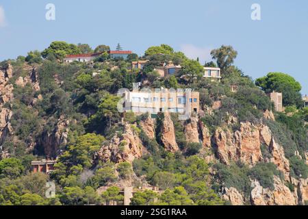 Una vista panoramica di case moderne arroccate su una collina rocciosa, circondate da vegetazione lussureggiante e alberi. Il cielo è limpido con poche nuvole, migliorando la b Foto Stock