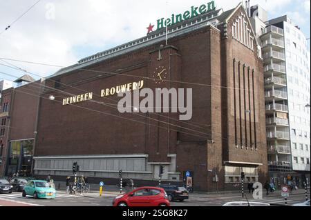 Un edificio in mattoni rossi con un grande cartello Heineken domina la scena di Amsterdam, forse un punto di riferimento per i turisti o un ex birrificio. Foto Stock