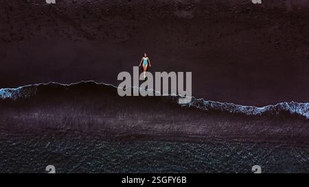 Vista aerea di una donna sdraiata su una spiaggia sabbiosa vicino all'acqua. Foto Stock