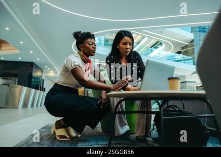 Due colleghi donne professionali che discutono di strategie finanziarie in un ambiente d'ufficio contemporaneo. Enfatizzare la crescita aziendale e la consulenza Foto Stock
