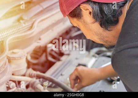 Il meccanico asiatico in un'officina di riparazione auto sta controllando il motore. Servizio di riparazione auto a casa. Vista posteriore, messa a fuoco selettiva. Foto Stock