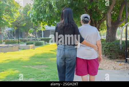 Giovane donna nel parco che indossa camminare con la vecchia nonna. Vecchia nonna che cammina con una bella figlia adulta. Vista posteriore, Copia spazio. Foto Stock