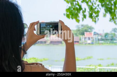 Donna asiatica scatta foto del fiume Chao Phraya, Thailandia, su uno smartphone, una vista dal retro. stile di vita attivo e impressioni Foto Stock