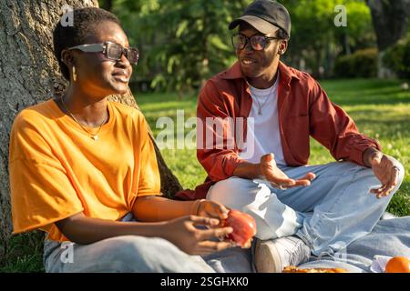 La coppia nera ama fare un picnic tranquillo, sedersi sulla coperta assaporando spuntini durante la conversazione, uscire all'aperto Foto Stock