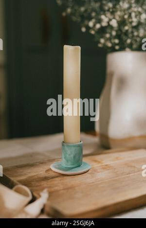 Una candela è accesa su un supporto verde su un tavolo di legno. La candela è gialla e il supporto è blu Foto Stock