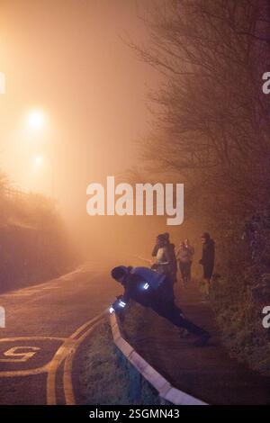 I corridori si estendono lungo una strada nebbiosa e poco illuminata durante la sera. I lampioni proiettano un caldo bagliore, sale Water Park, Manchester, Regno Unito Foto Stock