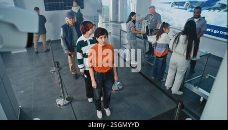 Checkpoint di sicurezza nel terminal dell'aeroporto: Coda di persone diverse, turisti alle procedure di screening TSA per il volo in aereo. Agenti di sicurezza che controllano i passeggeri. Messa a fuoco rack su telecamera CCTV. Angolo alto. Foto Stock