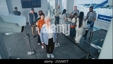 Checkpoint di sicurezza nel terminal dell'aeroporto: Coda di persone diverse, turisti alle procedure di screening TSA per il volo in aereo. Agenti di sicurezza che controllano i passeggeri. Messa a fuoco rack su telecamera CCTV. Angolo alto. Foto Stock