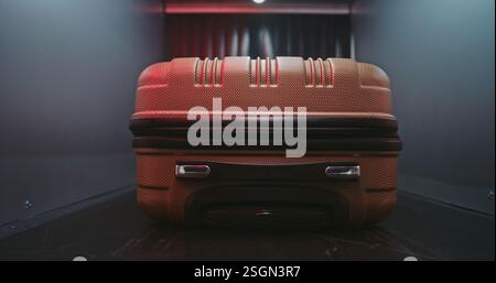 Controllo di sicurezza aeroportuale: Primo piano della valigetta che si sposta sul nastro trasportatore all'interno del moderno scanner a raggi X con rilevatore di metalli. Allarme a luce rossa relativo al rilevamento di un oggetto sospetto durante la procedura di scansione del bagaglio. Foto Stock