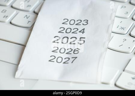 Elenco degli anni dal 2023 al 2027 su una ricevuta di cassa su una tastiera bianca, anno 2025 sulla ricevuta Foto Stock
