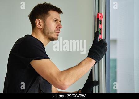 Costruttore professionista che utilizza una livella a bolla d'aria rossa per l'allineamento del telaio della finestra durante l'installazione. Riparazione di finestre bianche in pvc. Concetto di repai Foto Stock