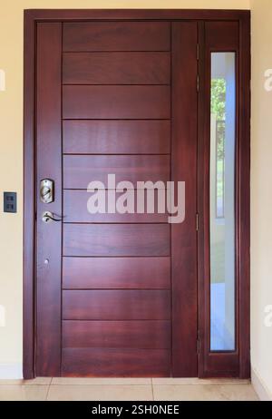 La porta in legno splendidamente lavorata presenta un design elegante con pannello in vetro che migliora l'estetica moderna dell'ingresso. Foto Stock