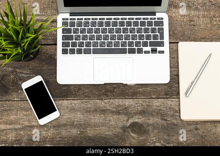 Configurazione dell'area di lavoro con laptop, smartphone e notebook su un tavolo in legno rustico Foto Stock