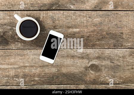 Tazza di caffè e smartphone su un tavolo in legno resistente agli agenti atmosferici durante una mattinata accogliente Foto Stock