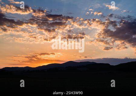 Tramonto sul campo con i raggi del sole dietro la collina, colorate nuvole torbide, paesaggi estivi serali. Zona agricola, Chocholna Slovacchia Foto Stock
