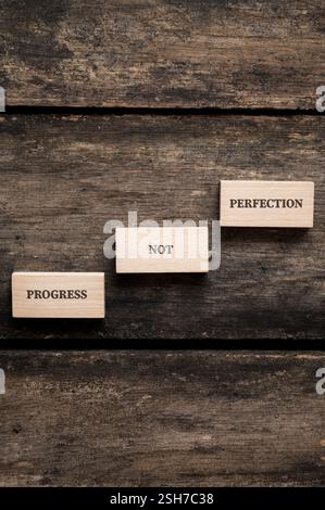 Tre blocchi di legno su una superficie rustica mostrano la frase PROGRESSO NON PERFEZIONE, simboleggiando la crescita e il miglioramento continuo rispetto alla ricerca di Foto Stock