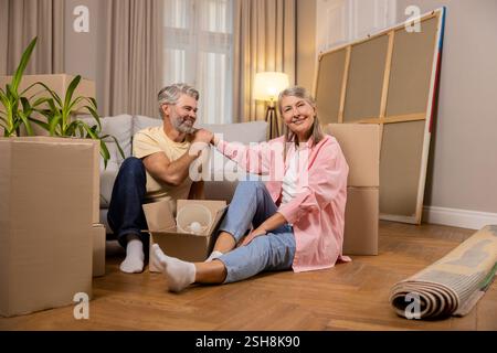 Uomo e donna allegri seduti circondati da scatole di cartone dopo il trasferimento Foto Stock