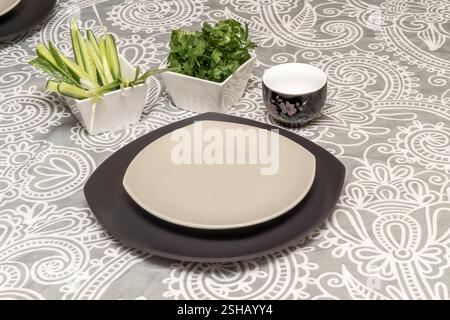 Piatti quadrati vuoti in stile giapponese su tovaglia con due ciotole quadrate con cetrioli, verdure di prezzemolo e tazza da tè Foto Stock