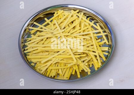 Spaghetti piatti crudi su una piastra di acciaio, su una superficie di legno chiaro. Foto Stock