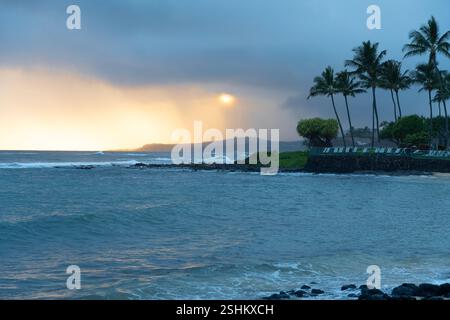 Una splendida scena serale a Poipu Beach sulla costa meridionale di Kauai, Hawaii, dove le calde sfumature dorate del tramonto si riflettono sulla calma dell'oceano Foto Stock
