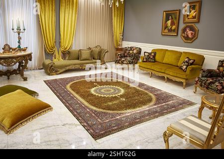 Sontuoso soggiorno con un tappeto persiano con medaglione d'oro, mobili d'oro decorati e decorazioni sfarzose. Foto Stock