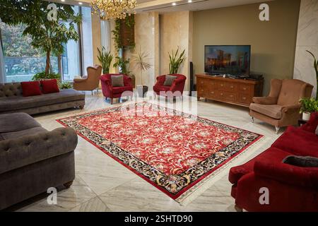 Soggiorno contemporaneo che presenta un tappeto persiano rosso con un intricato medaglione, pavimenti in marmo e lussureggianti piante interne. Foto Stock