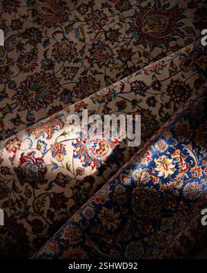 Primo piano di un tradizionale tappeto persiano con intricati motivi floreali in vivaci tonalità di rosso, blu e beige, illuminato da una luce naturale soffusa. Foto Stock