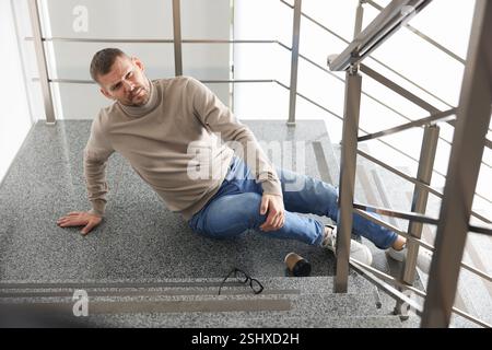 Uomo ferito sulle scale dell'edificio dopo la caduta. Incidente pericoloso Foto Stock