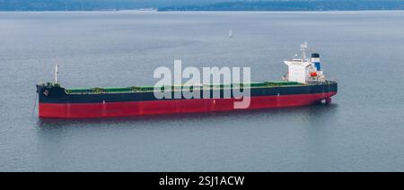 Grande nave da carico con scafo nero e rosso in calme acque costiere Foto Stock
