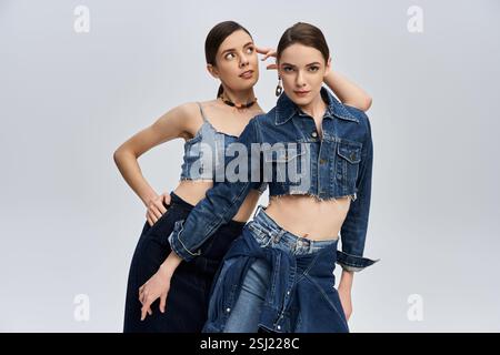 Due splendide sorelle esprimono i loro stili unici in abiti di tendenza in denim in un ambiente studio. Foto Stock