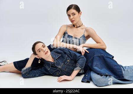 Due splendide sorelle gemelle si mettono in posa armoniosamente insieme, mostrando il loro senso della moda in denim. Foto Stock