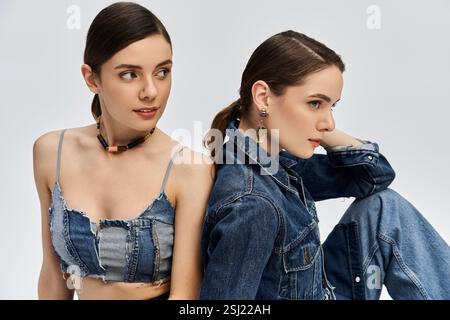 Due bellissime gemelle da donna modellano abiti in denim alla moda, trasudando eleganza e fascino in uno sfondo elegante. Foto Stock