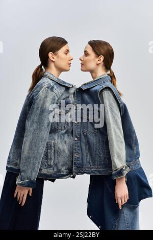 Due sorelle gemelle in giacche in denim coordinati si posizionano faccia a faccia, sottolineando il loro legame. Foto Stock