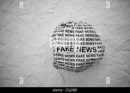 Palla di carta stropicciata con parole false notizie su frammenti di carta bianca sullo sfondo. Foto Stock
