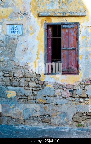 Vecchio edificio in pietra, fatiscente con vernice sbucciante e persiane rosse in legno sull'isola di Rodi, Grecia. Foto Stock