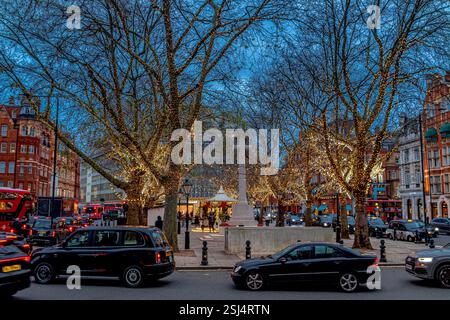 A Natale, le auto girano per Sloane Square con gli alberi nella piazza illuminati dalle luci natalizie, London SW1 Foto Stock