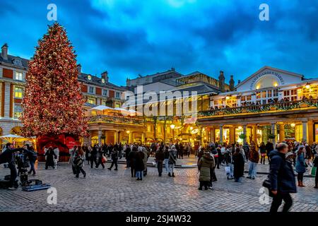 Gente che si riunisce intorno al grande albero di Natale al Covent Garden, un centro commerciale e di intrattenimento nel West End di Londra, Londra WC2 Foto Stock