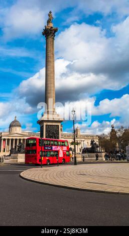 Ottima vista di un tipico autobus rosso che guida su Charing Cross e passa accanto al famoso monumento Nelson's Column in Trafalgar Square nella città di... Foto Stock
