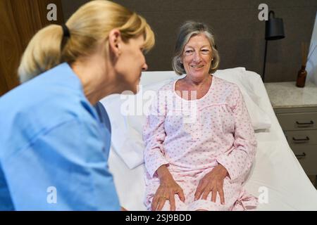 Un operatore sanitario comunica con un paziente anziano in Sleepwear in ambiente medico. Dimostra una capacità di cura, di guarigione e incentrata sul paziente Foto Stock