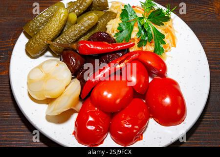 Un piatto vivace mostra un mix di verdure sott'aceto, tra cui pomodori, aglio e peperoni piccanti. L'aspetto fresco e la disposizione suggeriscono un soggiorno festivo Foto Stock