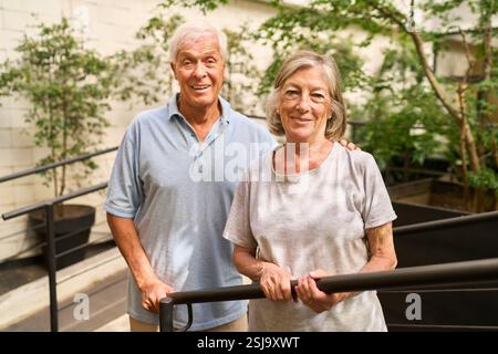 Un uomo e una donna anziani sorridono calorosamente mentre si godono il loro tempo in un ambiente verde all'aperto, mostrando calore e compagnia. Foto Stock
