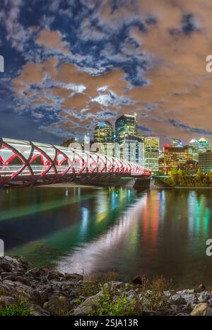 Una vista panoramica del Ponte della Pace a Calgary, Canada, al crepuscolo. Il ponte pedonale rosso attraversa il fiume Bow, con il moderno skyline della città. Foto Stock