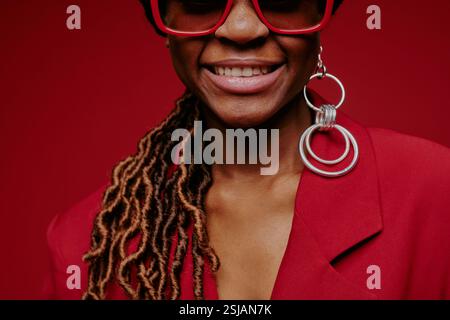 Ritratto di una donna sorridente che indossa un blazer rosso brillante con orecchini lunghi ed eleganti dreadlock. Primo piano di un afroamericano che guarda direttamente la fotocamera Foto Stock