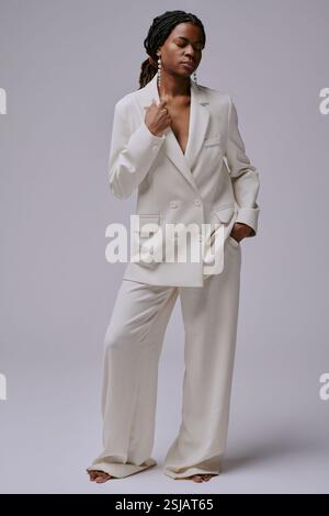 Donna vestita con una tuta bianca, in piedi con gli occhi chiusi. Sfoggia un look elegante e uno stile mentre posa su uno sfondo semplice Foto Stock