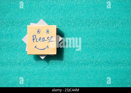 Una scritta a mano "Please" su una nota adesiva con divertenti volti sorridenti, collocata su uno sfondo luminoso. Un concetto allegro che rappresenta la gratitudine. Foto Stock