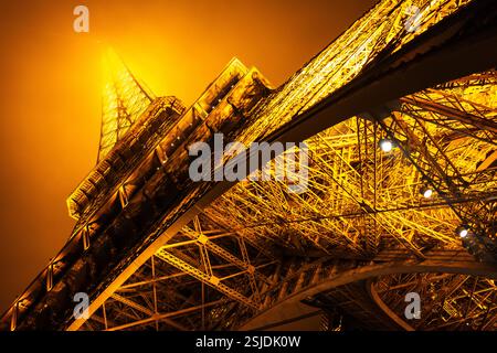 Vista ad angolo basso dal livello del suolo che guarda sulla Torre Eiffel illuminata, in una fredda e nebbiosa serata invernale. Parigi Foto Stock