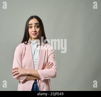 Giovane donna in piedi con le braccia incrociate e un'espressione scettica, isolata su sfondo grigio Foto Stock