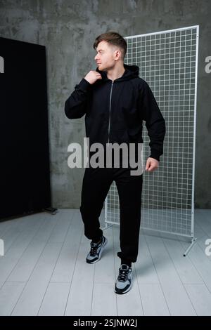 Un giovane uomo indossa un abbigliamento sportivo nero alla moda in un ambiente elegante e moderno Foto Stock